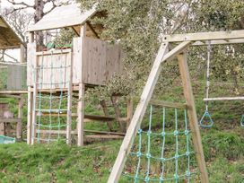 A wooden play structure with climbing nets and a swing set on grass at Cymryd Uchaf in Conwy