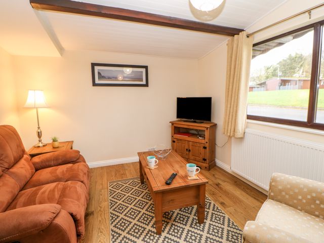 A living room with a brown sofa a beige armchair a wooden coffee table and a TV at Daffodil Lodge in Saltburn-by-the-Sea