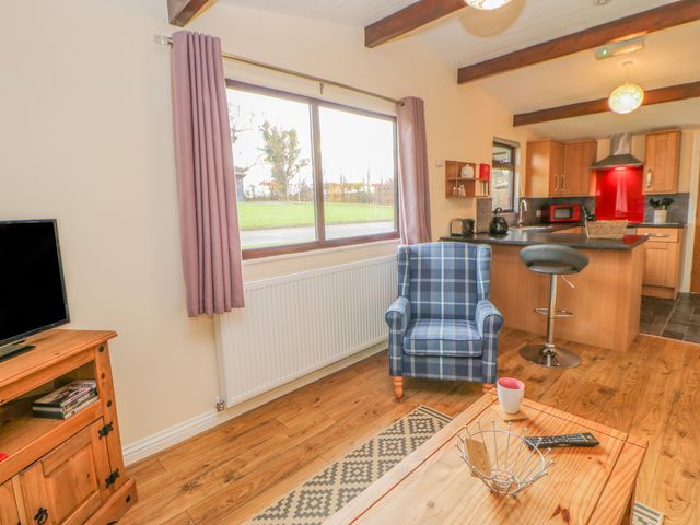 A living room with a blue plaid armchair wooden TV stand and a kitchen area with a breakfast bar and stool at Orchid Lodge in Saltburn-by-the-Sea