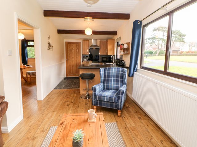 A living area with a blue plaid armchair a wooden coffee table hardwood flooring and an open kitchen with wooden cabinets at Foxglove Lodge in Saltburn-By-The-Sea