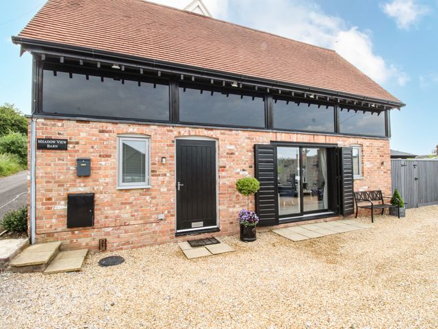 A brick barn with black door and large windows and a bench outside at Meadow View Barn in Bere Regis