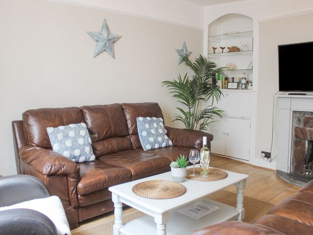 A living room with brown leather sofas a white coffee table with wine and plants and a built in bookshelf at Sandcastles 15A Fore Street in Salcombe