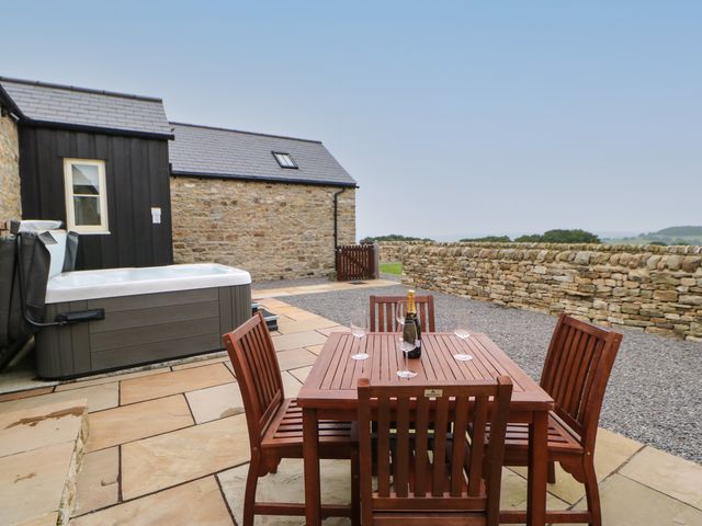 An outdoor patio with a wooden dining table and chairs a hot tub and a stone wall at Horsley Cottage in Waskerley near Consett