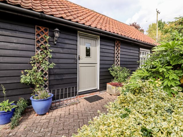 A black wooden exterior wall with a gray door and plants in blue pots at Courtyard Cottage Poplar Farm Barn Sweffling near Saxmundham