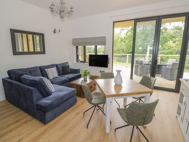 A living room with a navy blue sofa a wooden coffee table a square dining table with four chairs a wall-mounted TV and sliding glass doors showing outdoor chairs at The Barn in Droitwich Spa