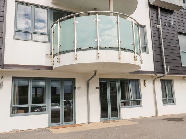 The exterior of a modern building with two doors numbered 6 and 7 and a balcony with glass panels above Apartment 7 in West Bay