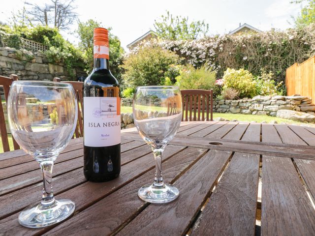 A bottle of Isla Negra wine and two empty wine glasses on a wooden table in a garden with chairs and stone walls at Clyd Fan in Harlech