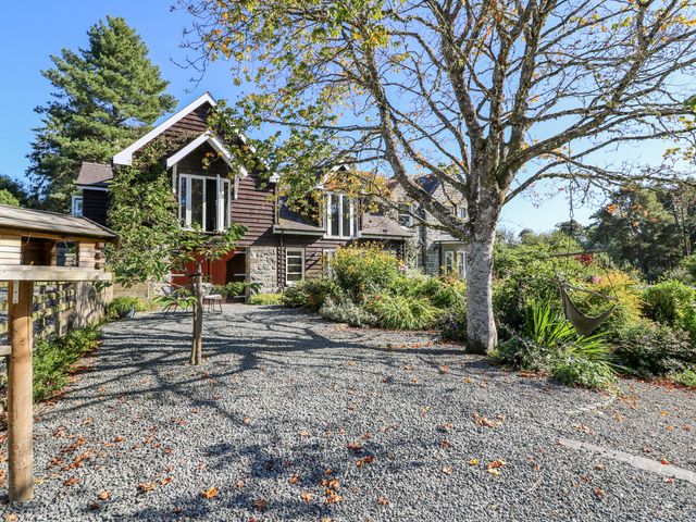 A garden with trees and gravel path outside a house with stone and wood walls at The Pheasantry in Builth Wells