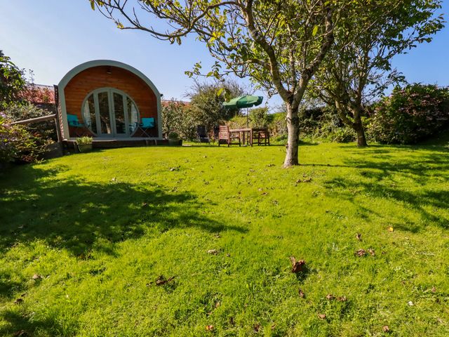 A garden with green grass trees a wooden pod with a round door and outdoor furniture at The Lamb Shack in St Teath