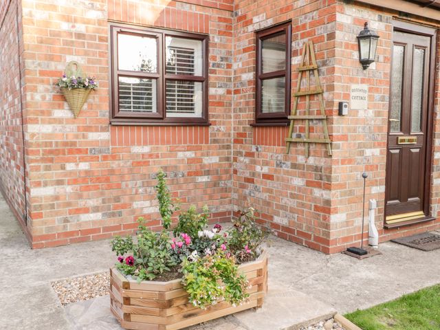 The entrance of a brick house with a dark brown door two windows a wooden planter with flowers and a wall basket with flowers at Rosewood Cottage in Flamborough