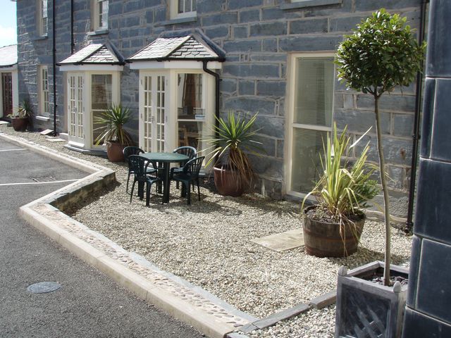 A small outdoor seating area with a round table and four chairs surrounded by potted plants in front of a stone building at Bwthyn Llechen in Porthmadog