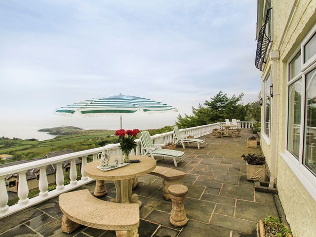 A stone patio with tables benches and umbrellas overlooking a coastal landscape at Amolca in Llaneilian