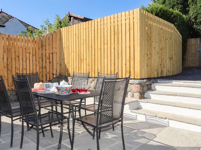 An outdoor patio area with a metal table and chairs and a wooden fence with steps leading up at Brook Cottage in Criccieth