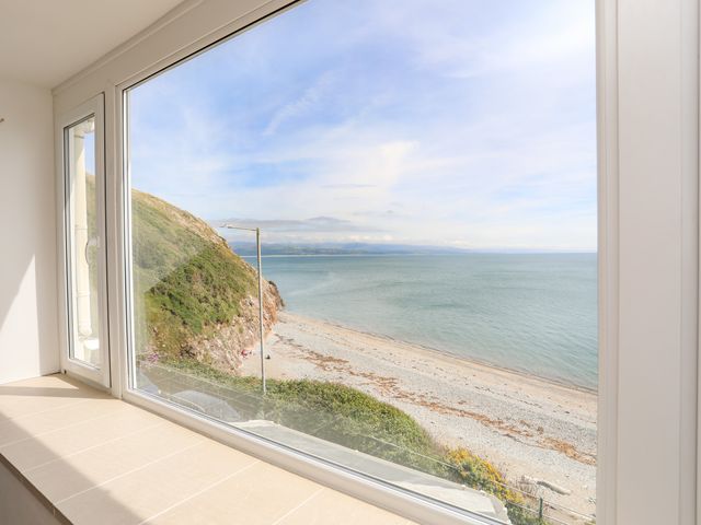 A large window with a view of a rocky beach and sea at Captains Rest in Criccieth