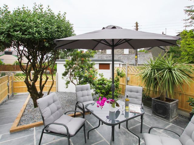An outdoor patio with a table and chairs under an umbrella surrounded by trees and plants at Cuckooland in Borth-Y-Gest