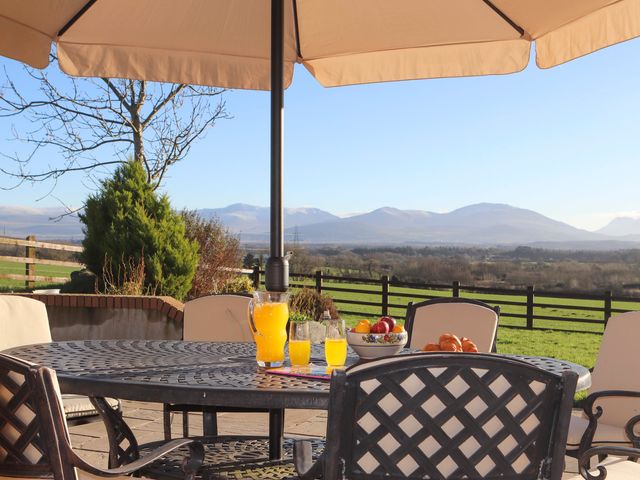 An outdoor patio with a table, chairs, umbrella, pitcher of orange juice, glasses, bowl of fruit, and croissants with mountains in the background at Dol Fraint in Star