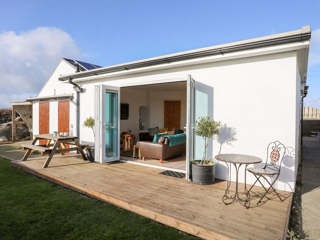 A wooden deck outside a white house with folding glass doors open to a living area at Farm Cottage in Cemaes Bay