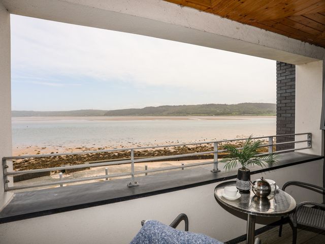 A balcony with a small table and two chairs overlooking a beach and hills at Four The Quay in Red Wharf Bay