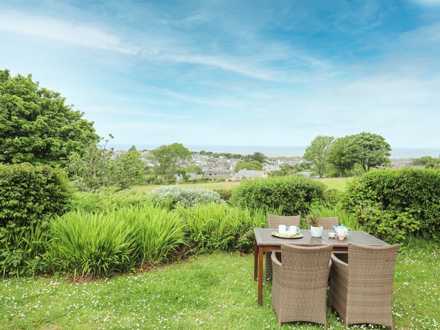 An outdoor garden with a wooden table and four wicker chairs overlooking houses and trees at Fron Fawr in Nefyn