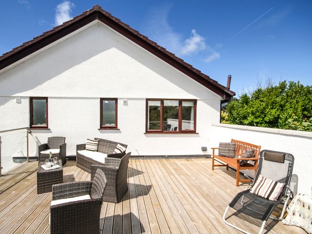 An outdoor wooden deck with wicker chairs, a sofa, a wooden bench, and a reclining chair at The Gables in Trearddur Bay