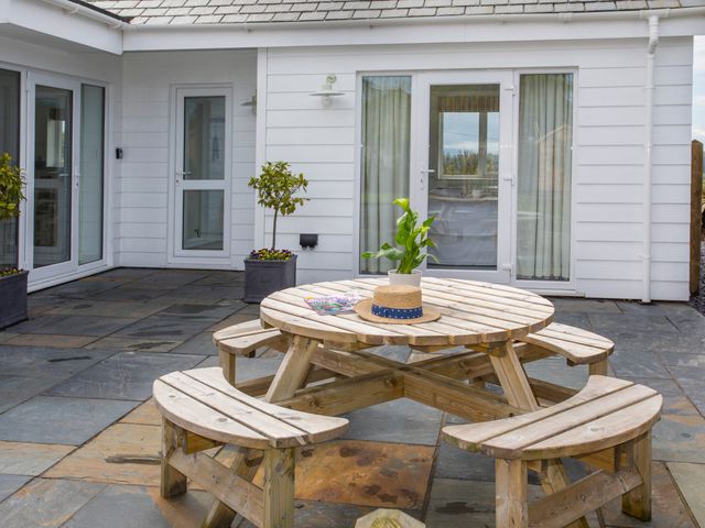 A patio with a round wooden picnic table and benches a hat and plant on the table potted plants near white doors and windows at Hafod Llangoed in Llangoed