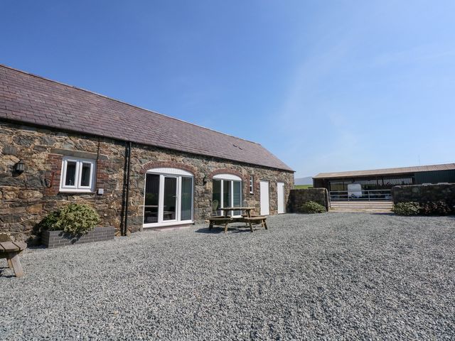 A stone building with white doors and windows a wooden picnic table and gravel ground at Hafod in Pontllyfni