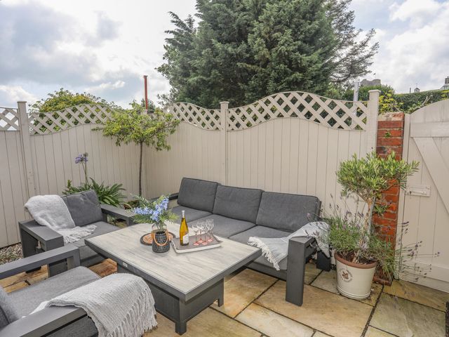 An outdoor patio with gray cushioned seating a wooden table glassware and potted plants at Maelgwyn Criccieth