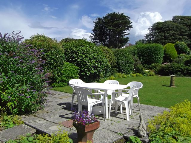 A garden with a white plastic table and four chairs on a stone patio surrounded by bushes and flowers at Mor Edrin in Criccieth