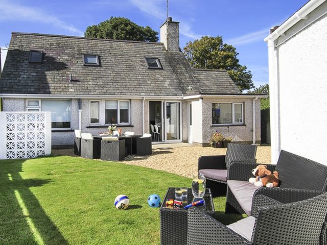 A backyard with outdoor seating furniture balls and a house with a stone roof at Perthi in Morfa Nefyn