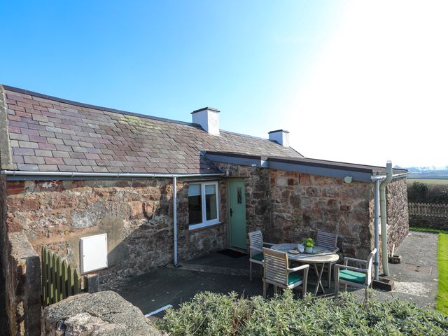 An outdoor patio area with a round table and four chairs next to a stone cottage at Tan Twr Farm Cottage in Dwyran
