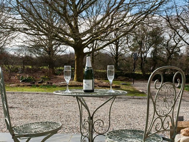 An outdoor metal table and two chairs with a bottle and two glasses on the table in a garden at Tyddyn Morthwyl in Criccieth