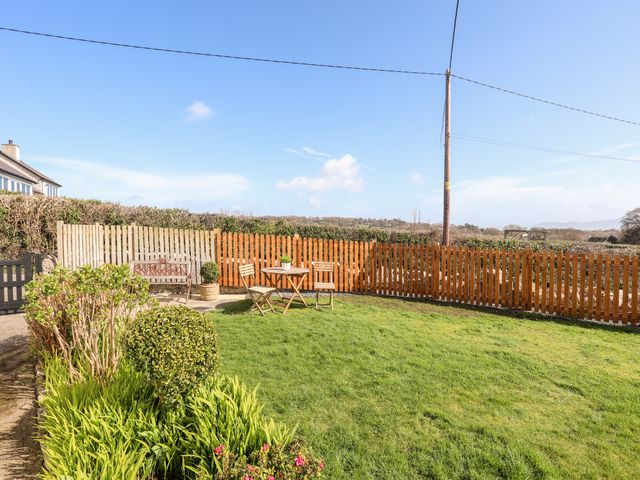 A fenced garden with a wooden bench table and chairs with plants and grass at Ty Hir in Llangoed