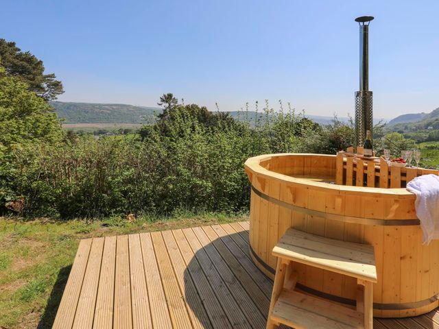 A wooden hot tub on a deck with a towel and glasses with countryside view at Ty'n y Cae in Llanbedr Y Cennin
