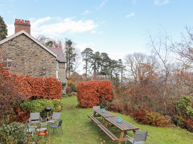 A garden area with outdoor chairs a barbecue and wooden picnic tables near a stone house at Ty'n y Cae in Llanbedr Y Cennin
