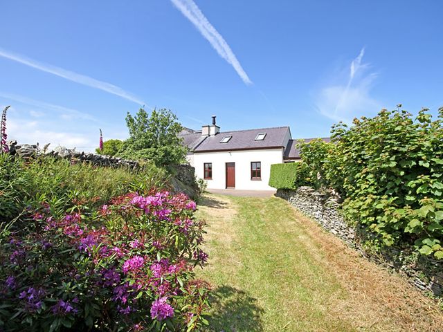 A garden path leading to a house with flowering bushes and stone walls at Tyn y Mynydd in Bull Bay