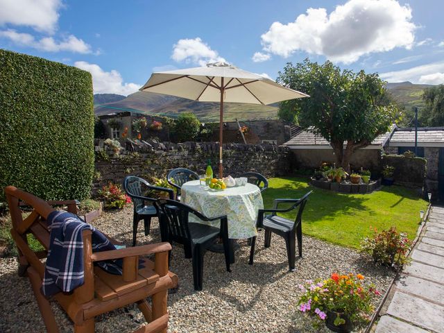 An outdoor garden with a table, umbrella, chairs, a bench, plants, and a tree at 17 Victoria Terrace - Perthi in Nantlle