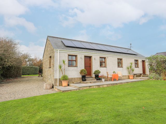 A single story house with solar panels on the roof a small patio with chairs and plants and a grass lawn at Y Beudy in Llanynghenedl