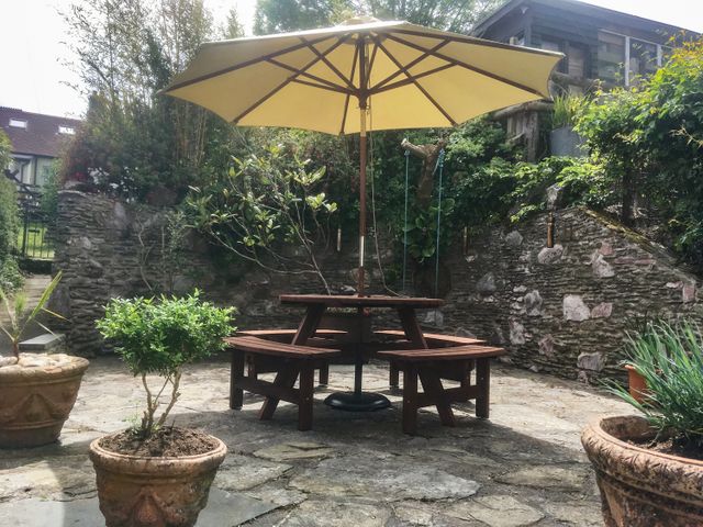 A circular wooden picnic table with benches and a large yellow umbrella in a stone patio garden at 3 Top View Cottages in Salcombe