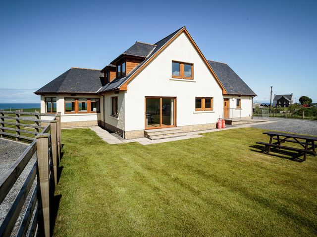 A large house with a grass yard a wooden fence and a picnic table at Corsewall Castle Farm Lodges in Kirkcolm