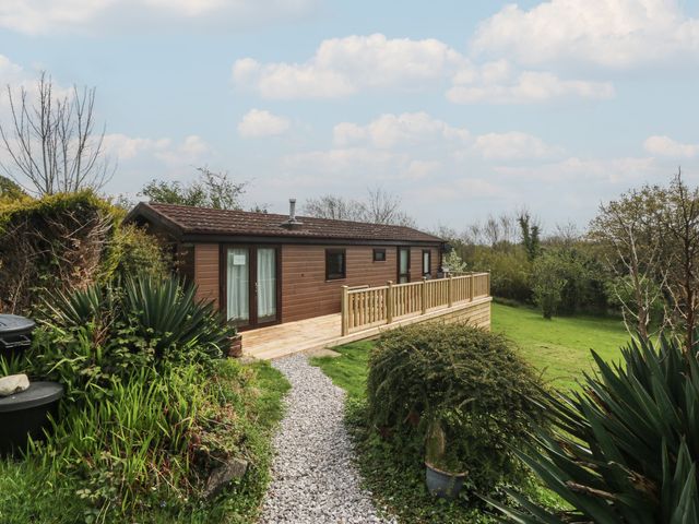 A wooden cabin with a deck and gravel path at Castell Chalet in Penrhos near Pwllheli