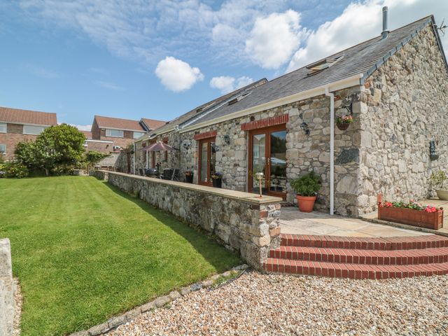 A stone barn conversion with glass doors and brick steps leading to a patio and lawn at Woodside Barns in St Austell