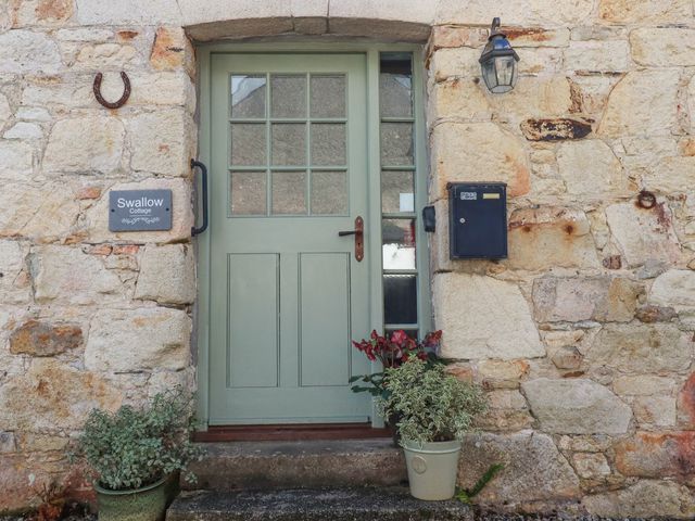 A stone wall with a green door flanked by potted plants a black mailbox and a sign reading Swallow Cottage at Swallow Cottage in Sticker