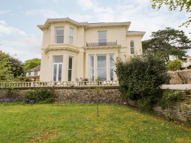 The exterior of a two story cream house with large windows and a garden with grass and bushes at Holcombe House in Torquay