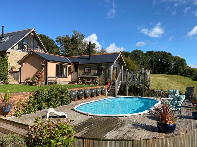 A backyard with a swimming pool wooden deck chairs and plants at The Hideout in Llangrove