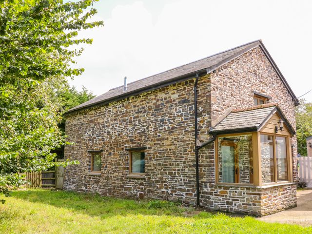 A stone house with a pitched roof and windows in a grassy yard at The Shippon in Barnstaple