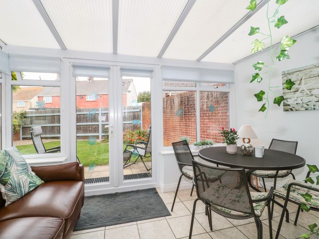 A conservatory with a brown sofa and round dining table with four chairs at Pebbles Foxglove Way in West Bay