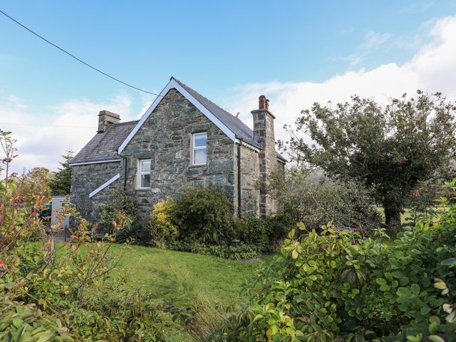 An exterior view of a stone house with a garden and trees at Glyn Morfa in Harlech