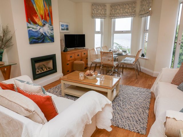 A living room with sofas, pillows, a coffee table, a television, and dining table with chairs at 1D Harbour View in Salcombe