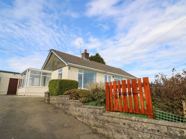 A bungalow with a tiled roof and front garden behind a red wooden fence at Gwynant in Pontrhydfendigaid
