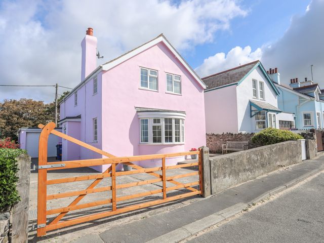 A pink two-story house with a wooden gate and concrete driveway at The Pink House in Rhosneigr